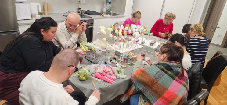 Kreativna radionica u udruzi, članovi sjede za stolom ispred kuhinje u udruzi, ukrašavaju se pisanice.