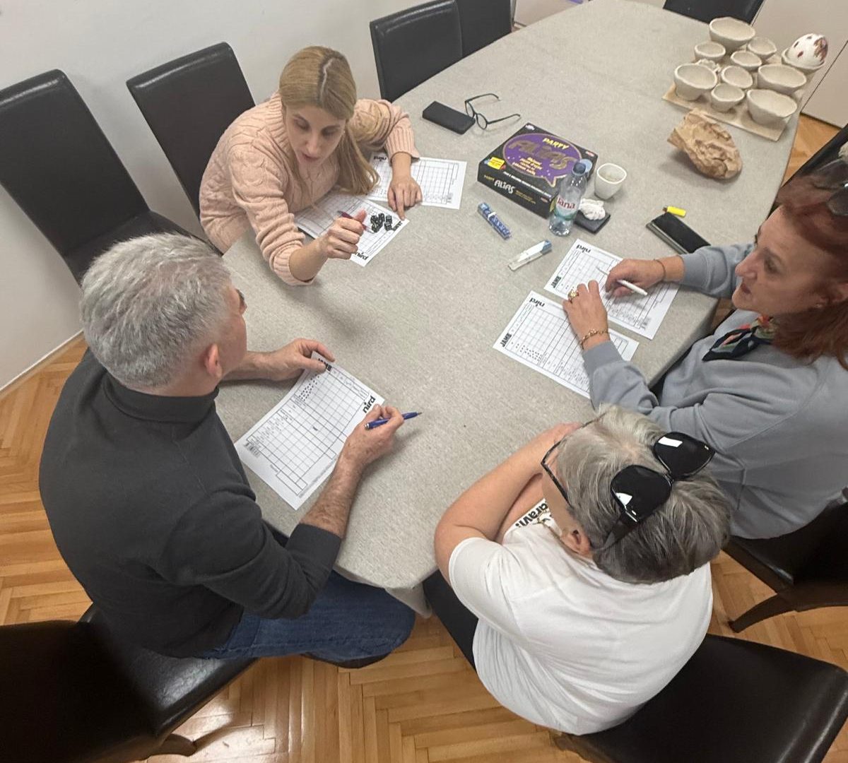 Ivana Mitar i videća pratiteljica Sanda s dvoje članova. Svi zajedno sjede za stolom i igraju društvenu igru Alias