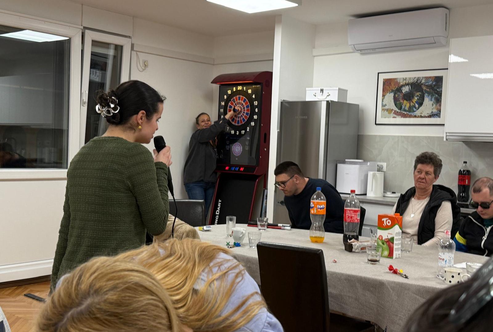 Anđela za mikrofonom, ekipa čeka red za pikado, ostali provode ugodno vrijeme u sali u razgovoru i druženju