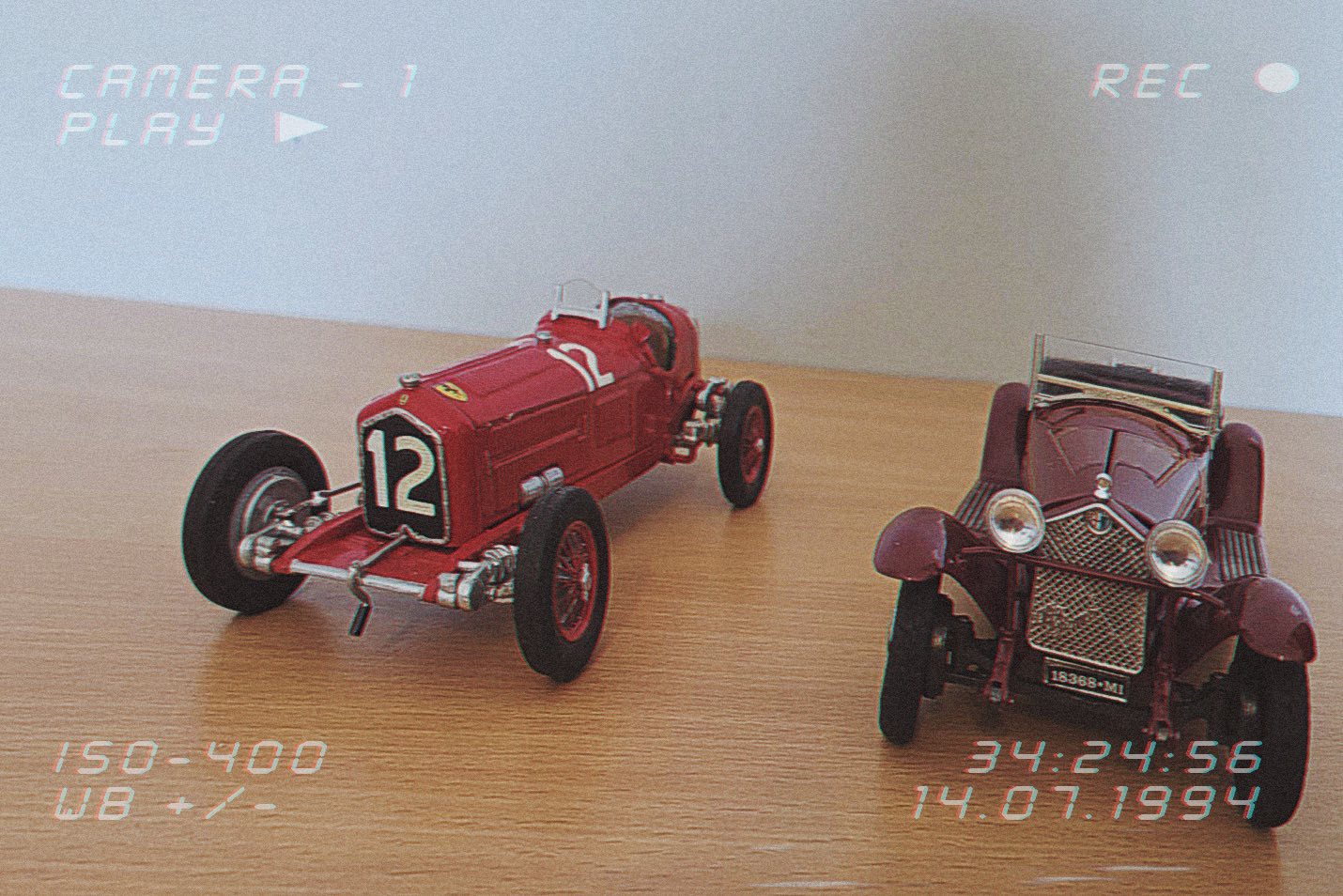 Dva starinska crvena trkaća autića stoje na drvenoj podlozi. Slika ima retro efekt koji podsjeća na snimku starom kamerom.