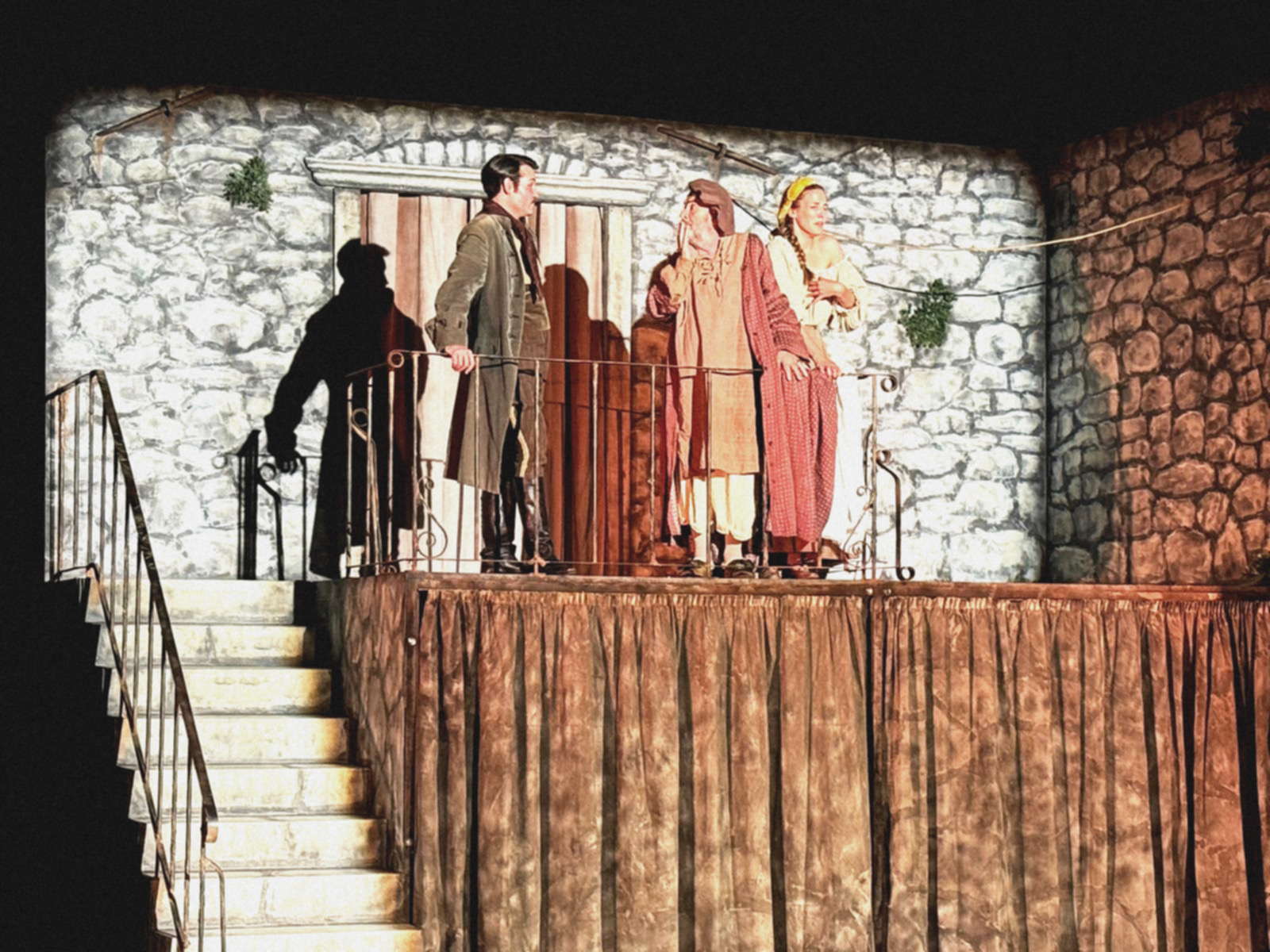 Isječak iz predstave Grintalo. Scenografija prikazuje staru dalmatinsku kuću na čijoj balaturi se nalaze tri glumca. 