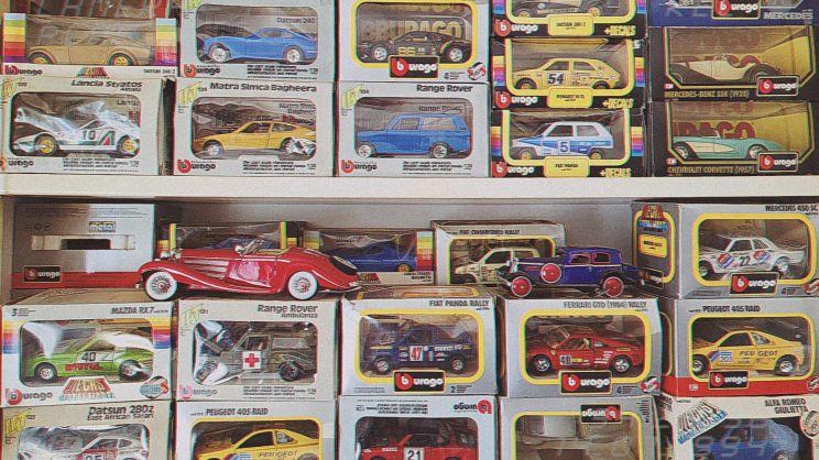 Na policama je izložena kolekcija zapakiranih Bburago metalnih modela automobila, različitih marki i boja, među kojima su klasični i trkaći automobili brendova poput Peugeota, Range Rovera i Ferrarija.